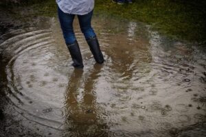 person with rain boots standing on body of water