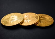three gold-colored bitcoins on black surface