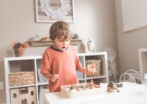 boy in orange crew neck t-shirt standing in front of white wooden table with cupcakes