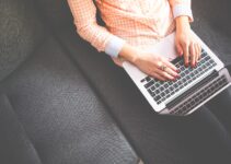 Person Sitting on Gray Sofa While Using Macbook