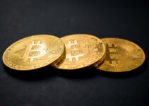 three gold-colored bitcoins on black surface