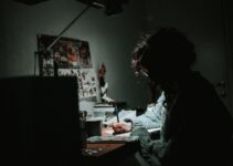 low light photography of woman in gray knit sweatshirt writing on desk