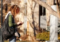 woman in green long sleeve shirt and black pants standing near brown tree during daytime