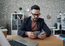 a man sitting at a table with a laptop and money