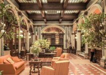 A luxurious hotel lobby featuring elegant architecture, rich decor, and comfortable seating under a stained glass ceiling.