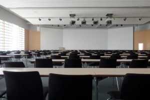 Spacious contemporary conference room with rows of tables and chairs, ready for meetings.