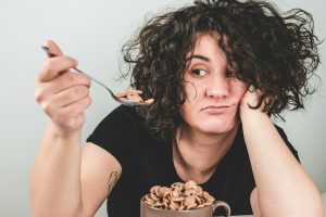 woman with messy hair wearing black crew-neck t-shirt holding spoon with cereals on top