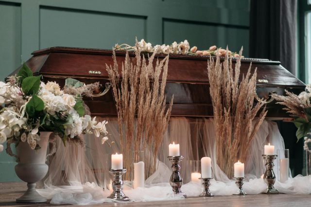 A serene funeral setting with a wooden casket, floral decorations, and soft candlelight indoors.