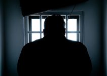 Dark silhouette of a man in a prison cell, backlit by window bars.