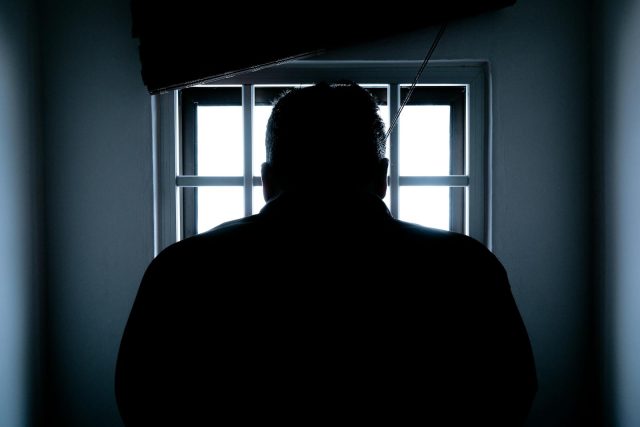 Dark silhouette of a man in a prison cell, backlit by window bars.