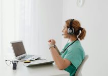 A female doctor using a laptop for an online consultation, wearing a headset in a bright office.