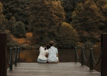 man in white dress shirt sitting on brown wooden dock during daytime