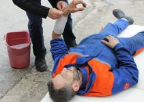 Injured worker receiving first aid on-site with arm bandage applied.