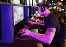 A focused gamer plays on a high-performance PC in a modern cyber café setting under purple lighting.