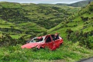 A red wrecked car lies abandoned in a scenic green valley, highlighting rural decay.