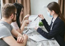 Three adults discuss a home insurance policy at a meeting table indoors.