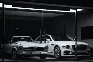 A vintage Mercedes-Benz and a modern Bentley parked behind a glass storefront