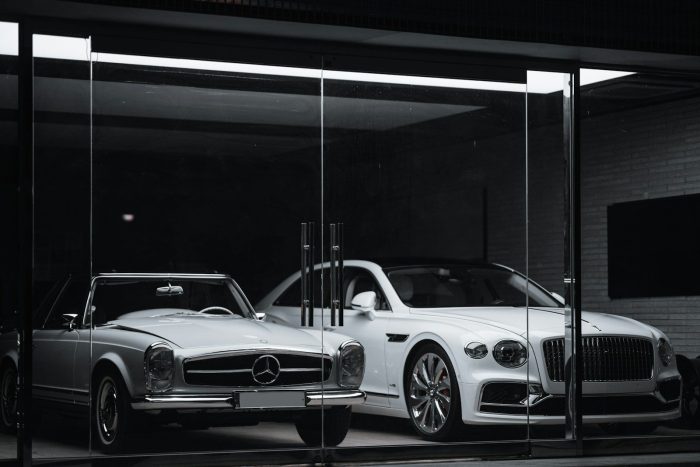 A vintage Mercedes-Benz and a modern Bentley parked behind a glass storefront