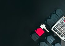A silver key, a red house model, and a calculator on a black surface