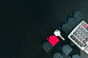 A silver key, a red house model, and a calculator on a black surface